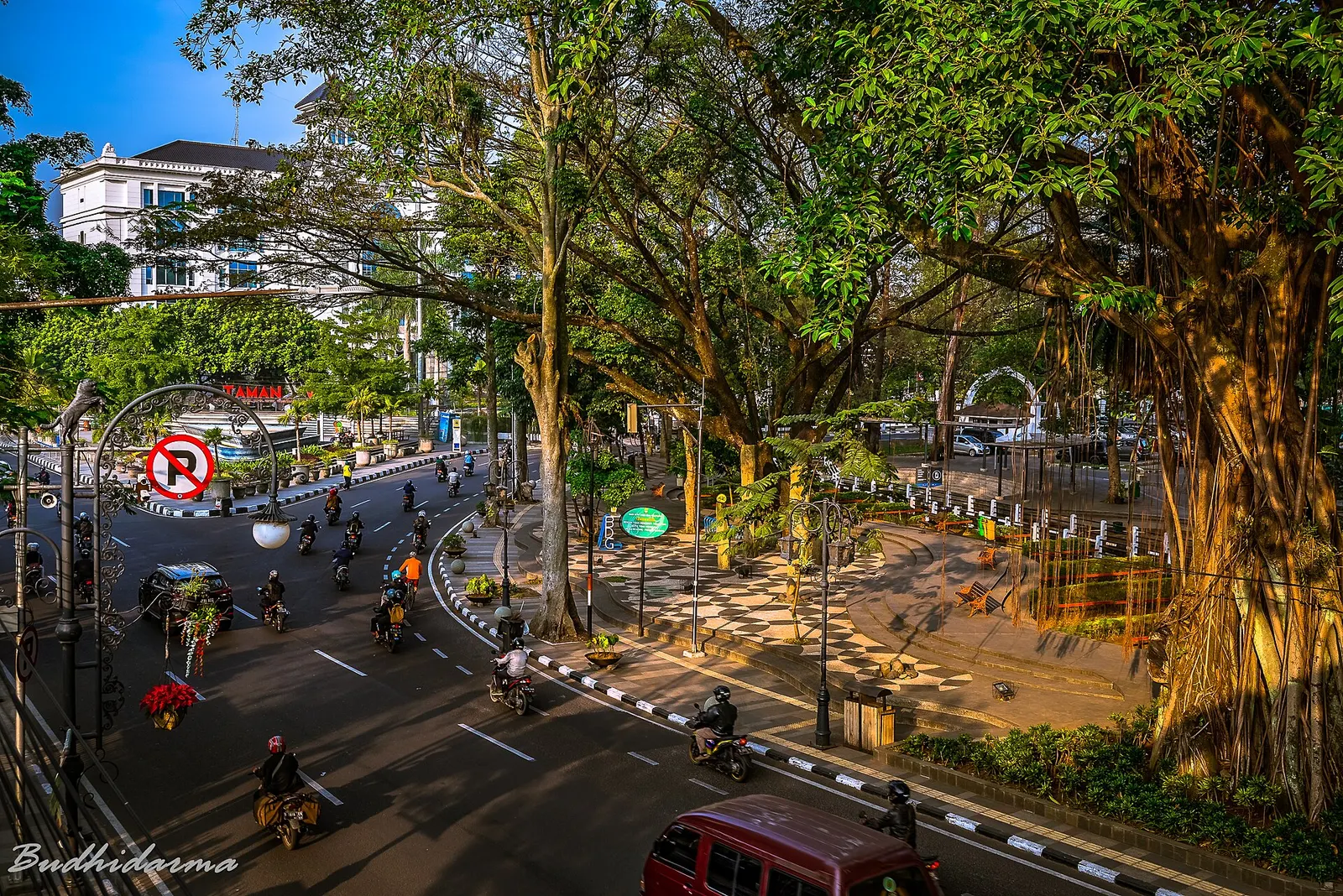 Tree-lined street in central Bandung with motorbikes at a bend